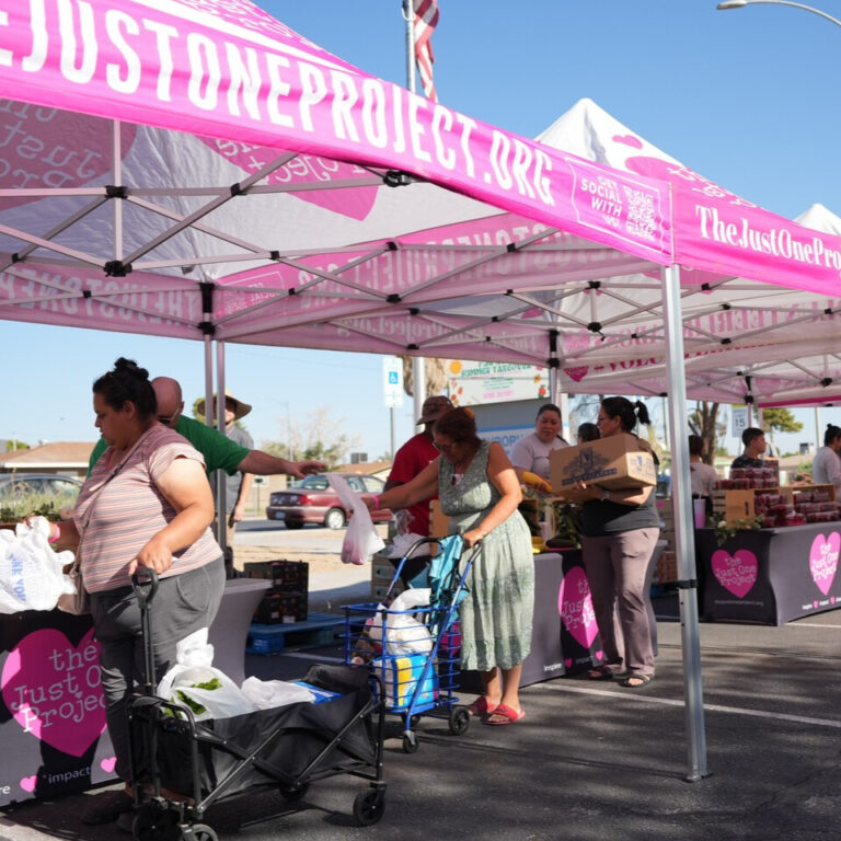 Community members receive fresh produce at a pop-up farmers market hosted by The Just One Project, with volunteers distributing food under TJOP tents to support local families.