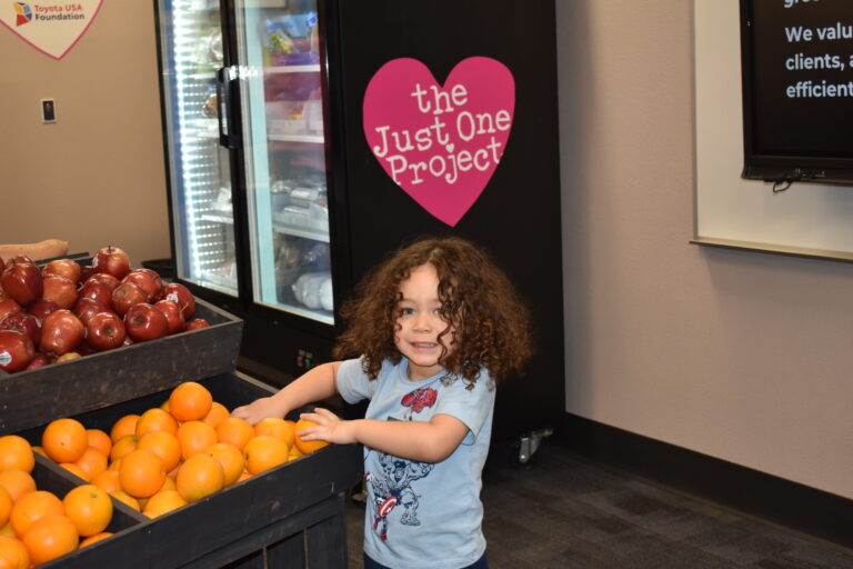 Child selecting fresh oranges at The Just One Project community market in Las Vegas, highlighting access to free groceries for local families.