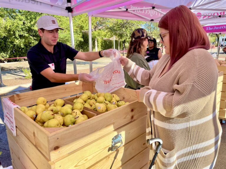 The Just One Project volunteer provides fresh produce to a participant at the Food as Medicine Farmers Market, improving food access and nutrition in Southern Nevada.