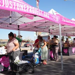 Community members receive fresh produce at a pop-up farmers market hosted by The Just One Project, with volunteers distributing food under TJOP tents to support local families.
