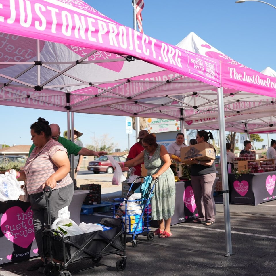 Community members receive fresh produce at a pop-up farmers market hosted by The Just One Project, with volunteers distributing food under TJOP tents to support local families.