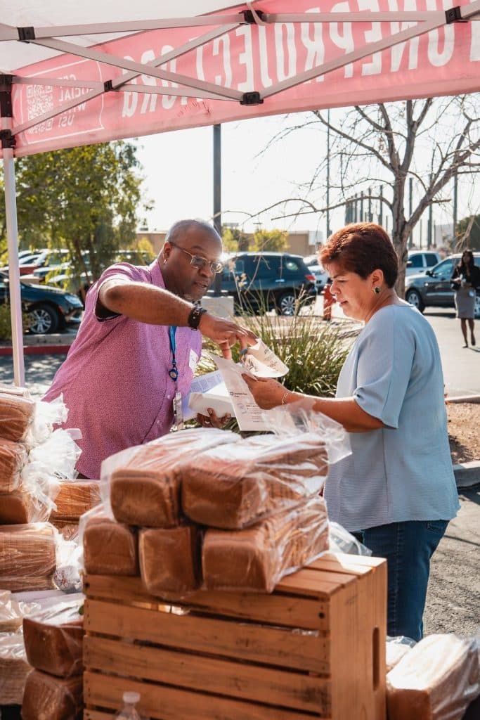 A man in a pink shirt hands a woman in blue a document under a tent with reversed text.
