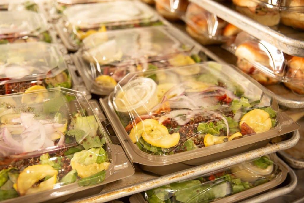 Rows of clear plastic containers hold fresh salads with lettuce, red onions, and yellow squash.