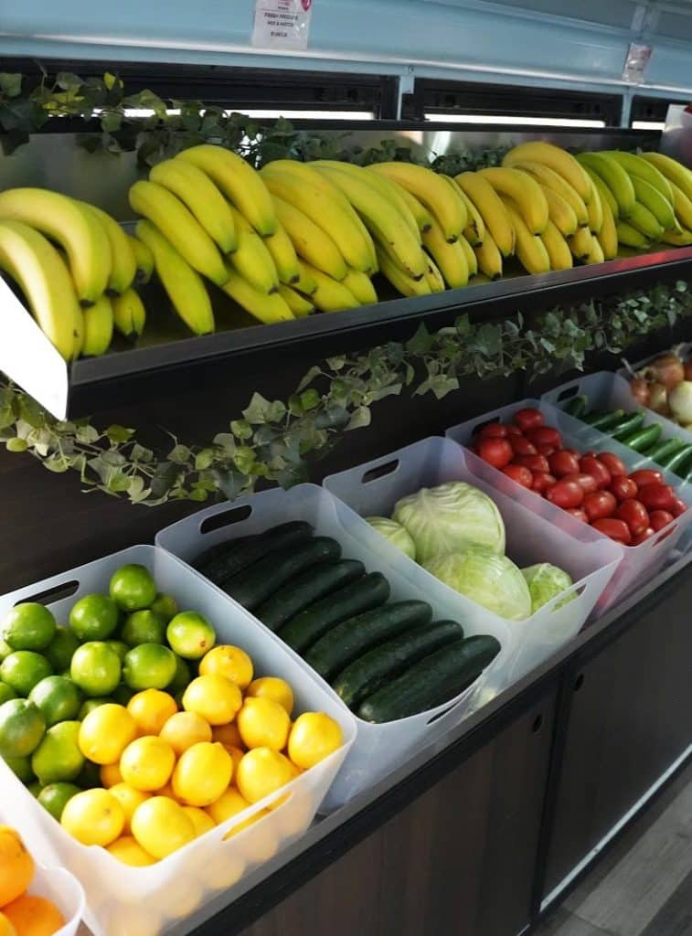 Rows of bananas, green and yellow, sit above bins of limes, lemons, cucumbers, cabbage, and tomatoes.