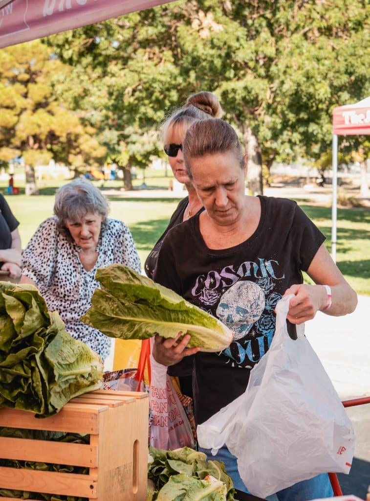 A woman in a "COSMIC" skull t-shirt puts romaine lettuce into a plastic bag at a market.