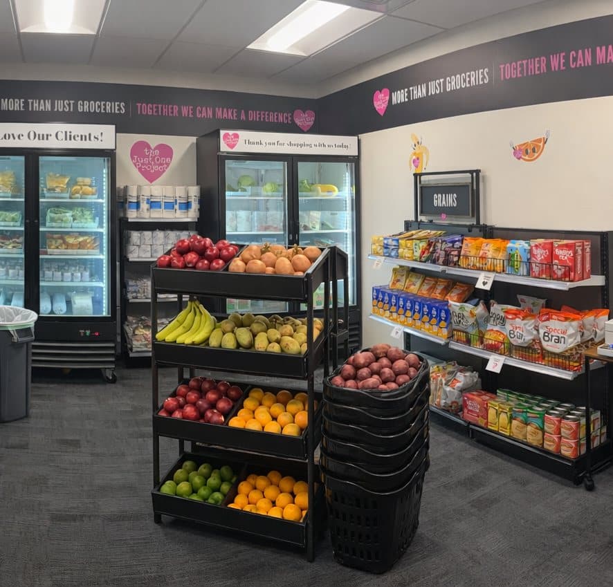 A well-stocked food pantry with fresh fruit, refrigerated items, and packaged goods; text reads "MORE THAN JUST GROCERIES TOGETHER WE CAN MAKE A DIFFERENCE."