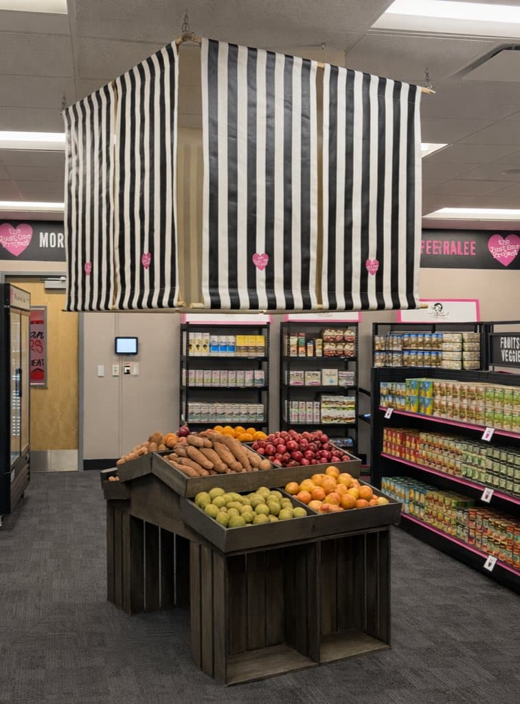 A grocery store with a wooden produce stand displaying fruits and vegetables, and shelves stocked with various items.