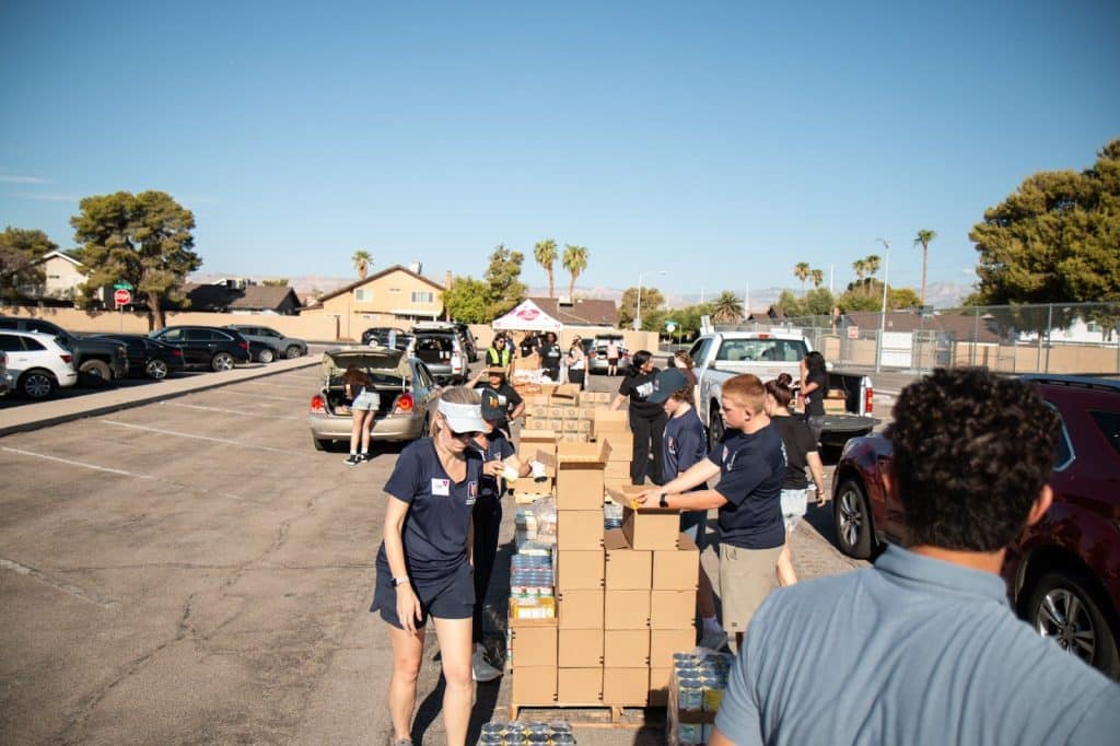 Volunteers load boxes of food and supplies into cars at an outdoor distribution event.